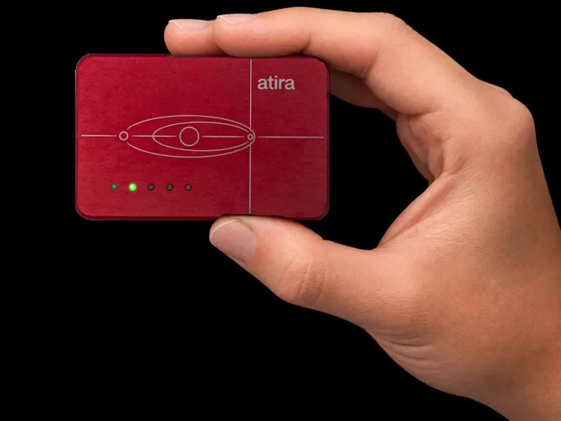 A hand holding the Binho Atira, a compact machined-aluminum USB debug probe, powering on with its five status LEDs lighting up